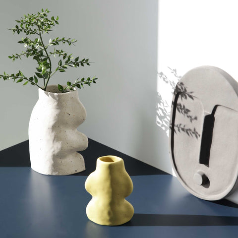 2. Lifestyle image of Fluxo Ceramic Vase in white with greenery, alongside a yellow vase and decorative wall piece