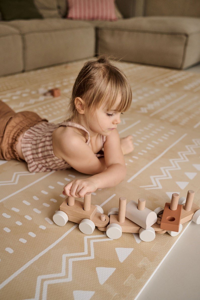 1. Child playing with wooden train on OLYA KIDS Boho sand puzzle playmat in a cozy living room