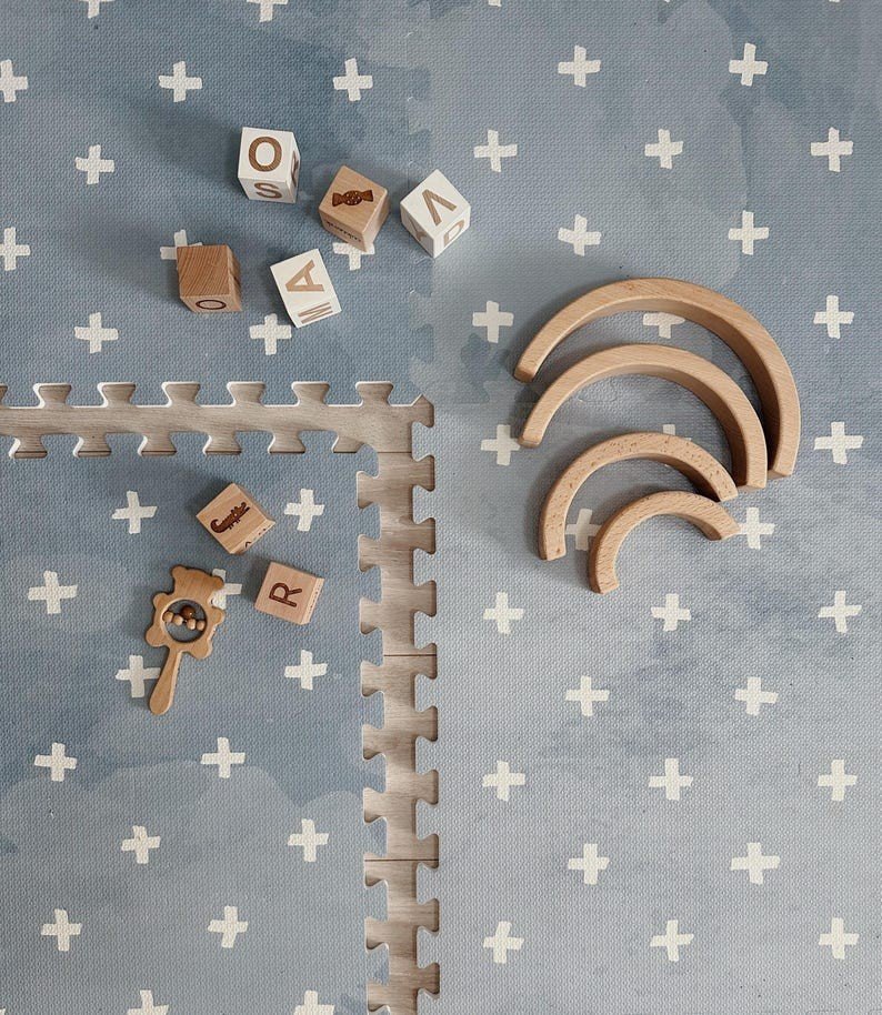 3. Close-up of OLYA KIDS Cross Azure foam puzzle playmat with wooden blocks and toys on blue background with white crosses