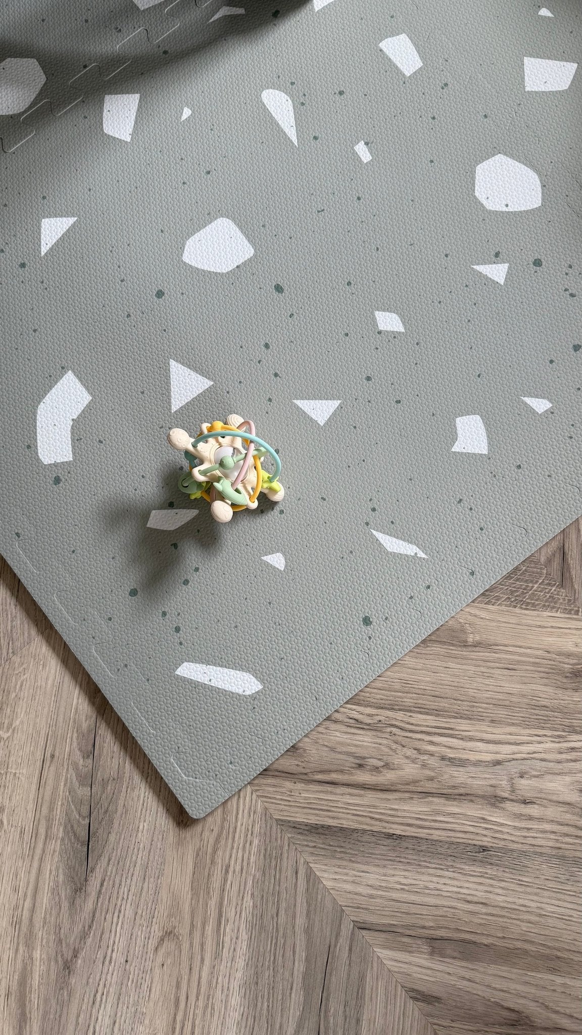 7. Close-up of OLYA KIDS Terrazzo Sage foam playmat with toy on wooden floor.
