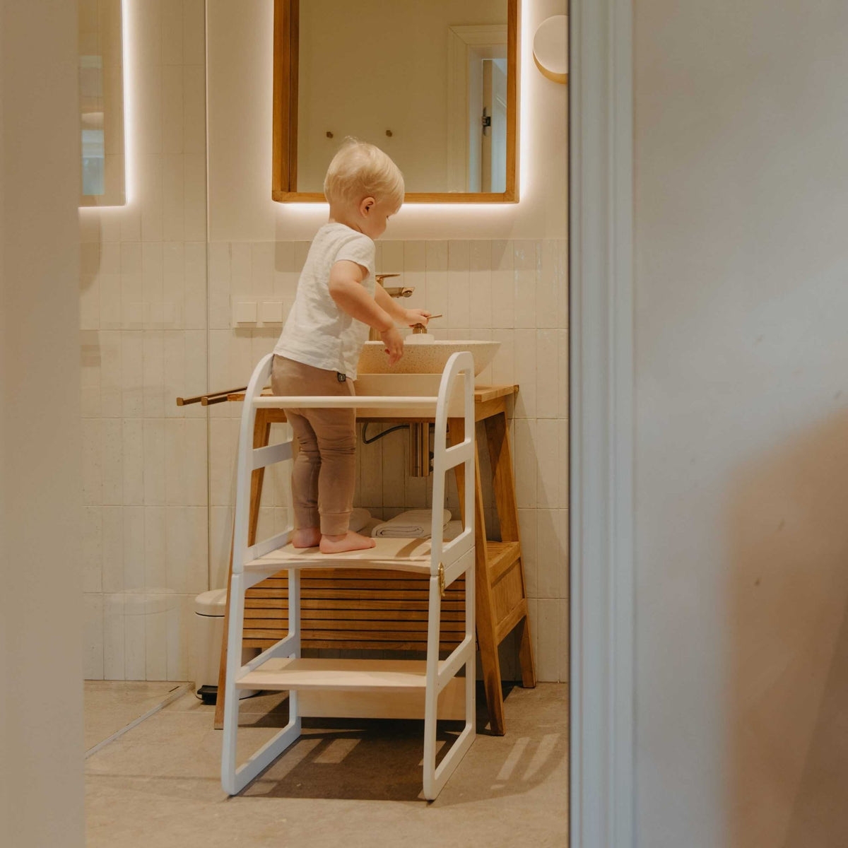 7. Child using white kitchen tower at bathroom sink