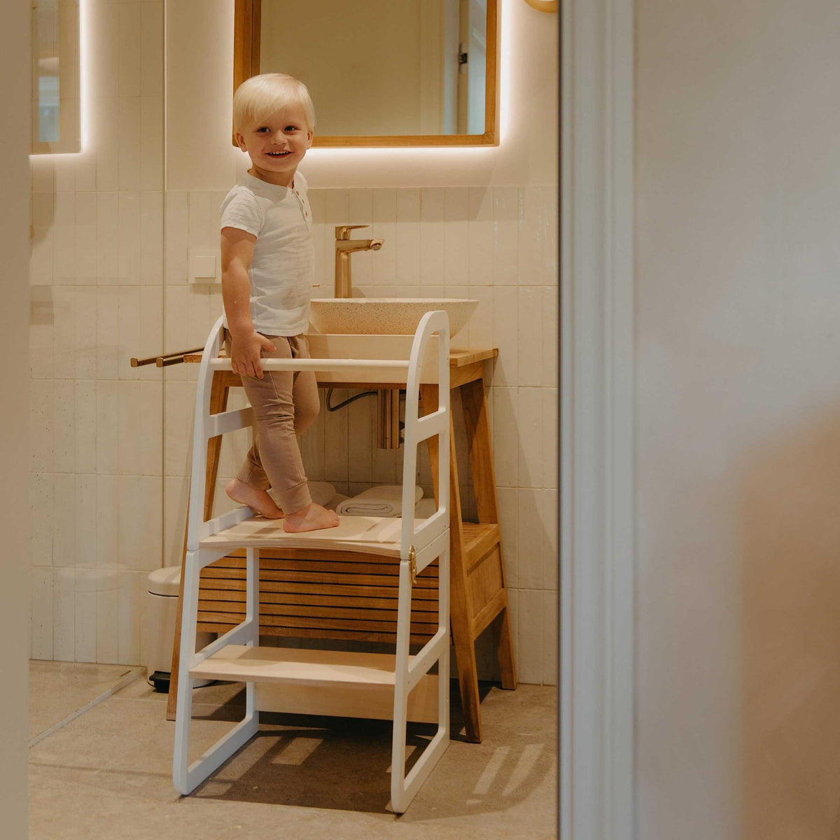 9. Child standing on white kitchen tower in bathroom setting