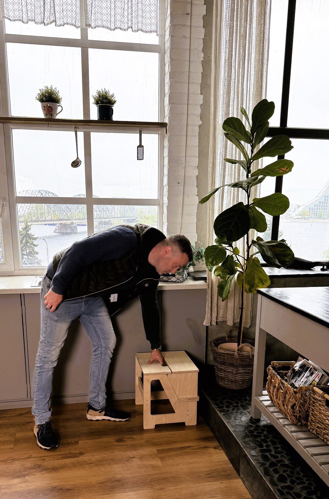 1. Man placing wooden folding seat and climbing helper in kitchen corner near plant