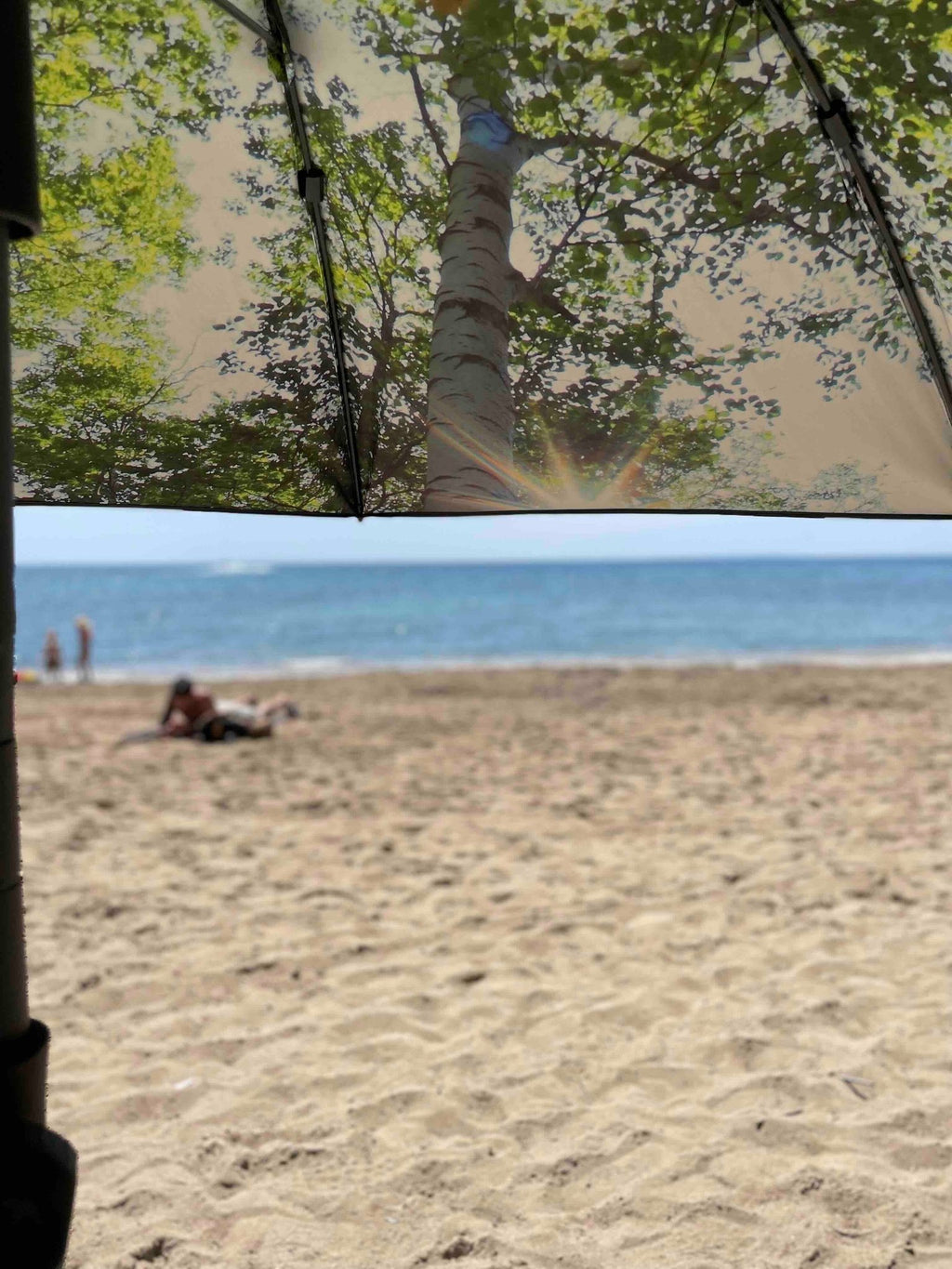 2. HAPPYSWEEDS forest-themed parasol with tree print offering shade on beach with people in background