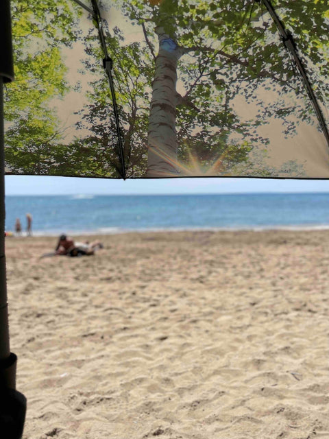 2. HAPPYSWEEDS forest-themed parasol with tree print offering shade on beach with people in background