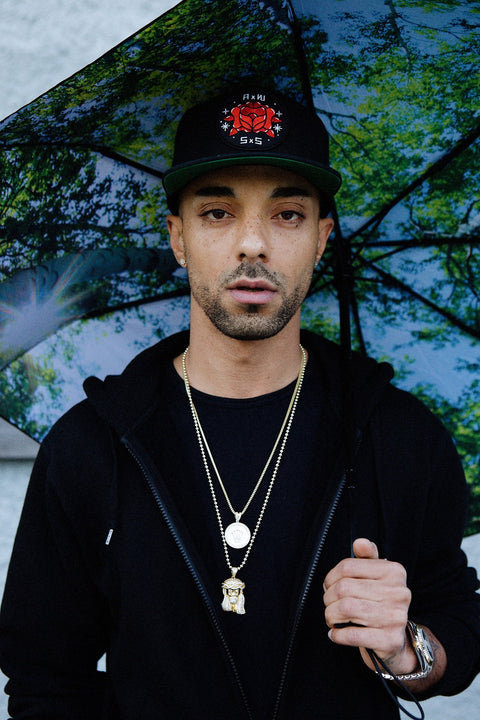 1. Man holding forest print umbrella with green and black design, wearing black jacket and cap