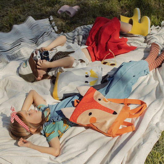 2. Muni kids fox backpack on picnic blanket with children, highlighting outdoor adventure setting