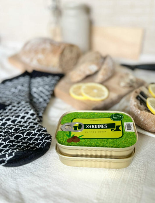 1. French Sardine Unisex Socks in a Can by SEIK, shown with black and white pattern socks and bread, lifestyle setting