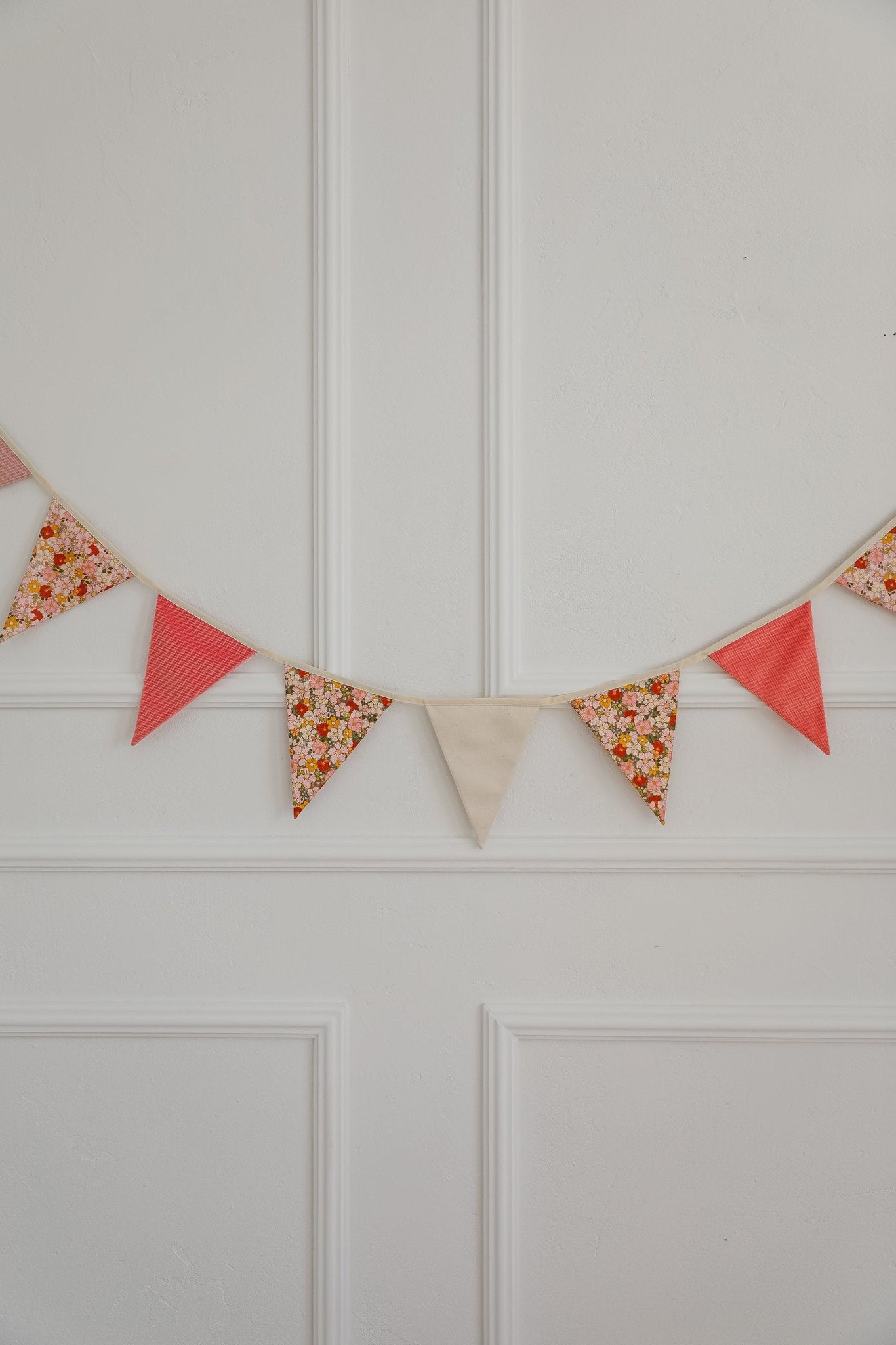 1. Decorative garland with pink, floral, and beige pendants hanging on a white paneled wall