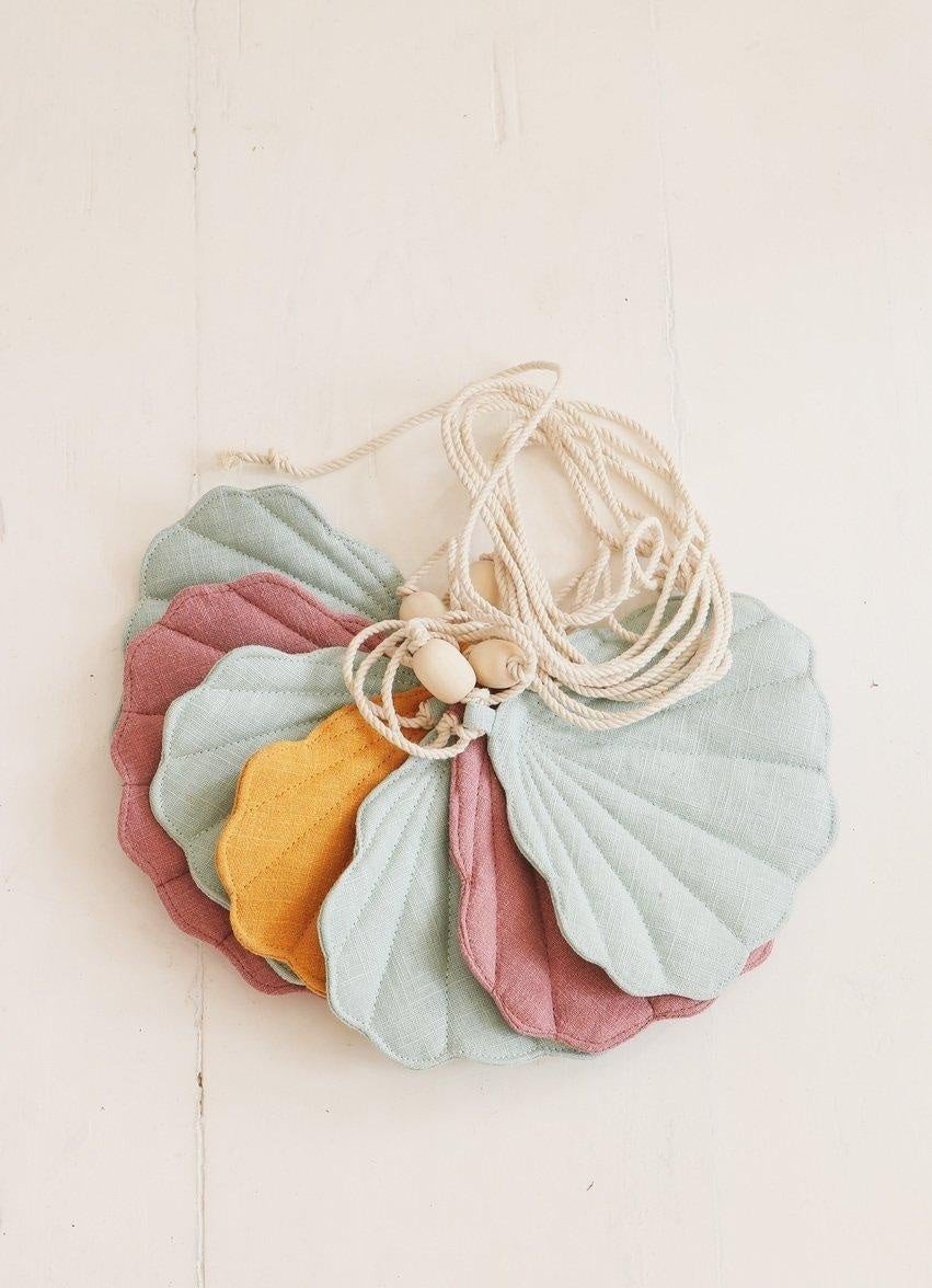 1. Flat lay of moi mili Shell Garland with mint, dirty pink, and mango linen shells on a cotton string with wooden beads on a light background