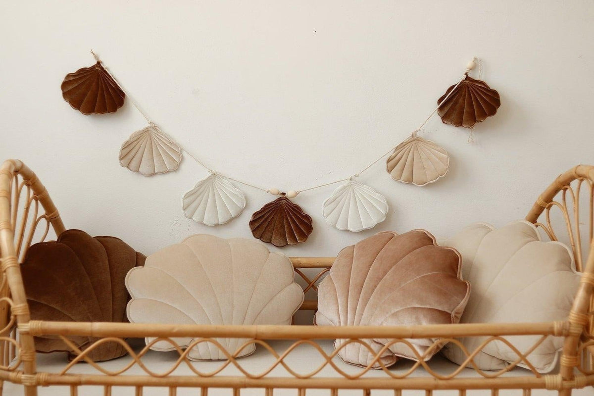 3. Beige and brown shell garland displayed above a rattan crib with matching shell cushions in a nursery