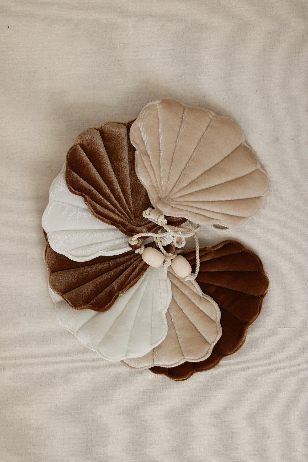 6. Flat lay of overlapping velvet shell garland in brown, beige, and cream with wooden beads on a beige background