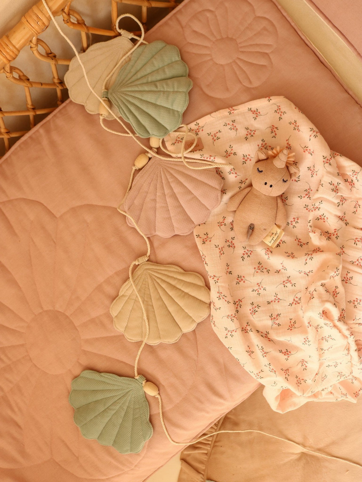 4. Flat lay of pastel shell garland on a pink quilted mat with a plush toy and floral blanket
