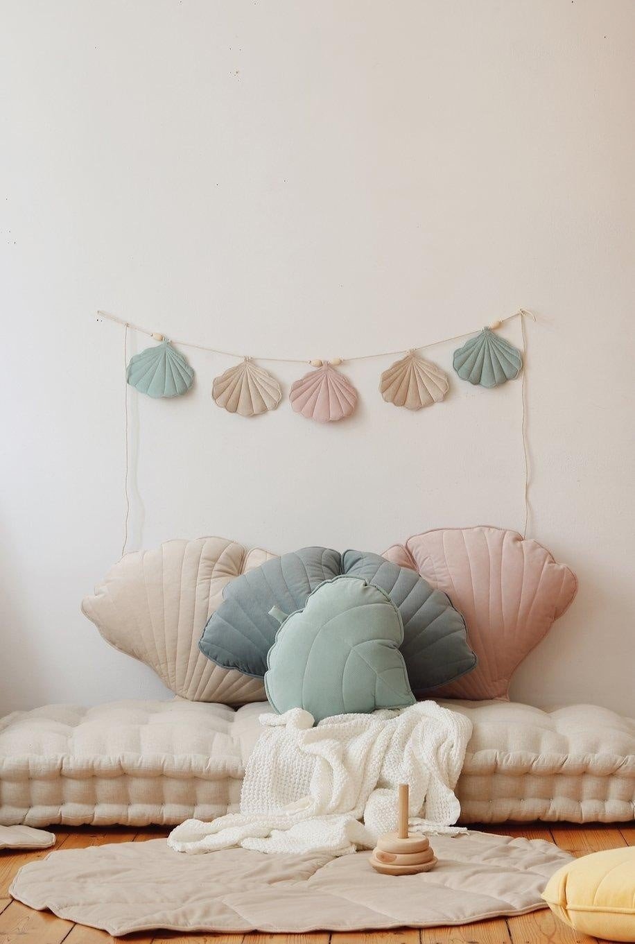 1. Shell garland with pastel velvet pendants hanging above a cozy seating area with shell-shaped cushions in a child's room