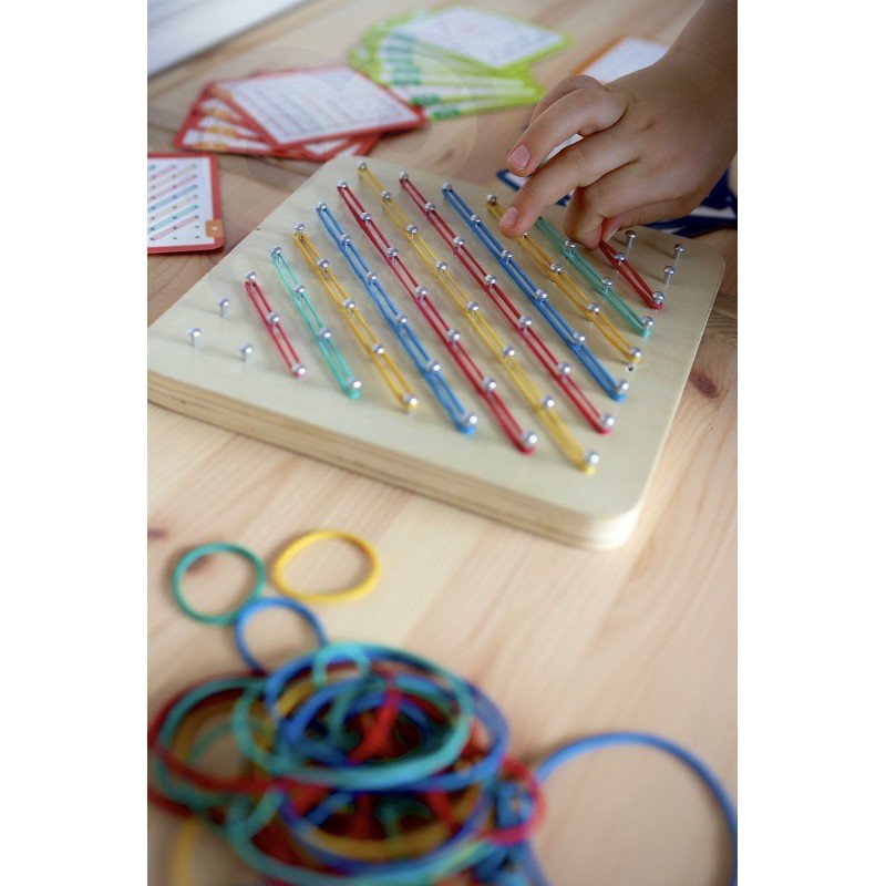 6. Child's hand placing rubber bands on Woopie Green Geoplan board with colorful bands scattered nearby