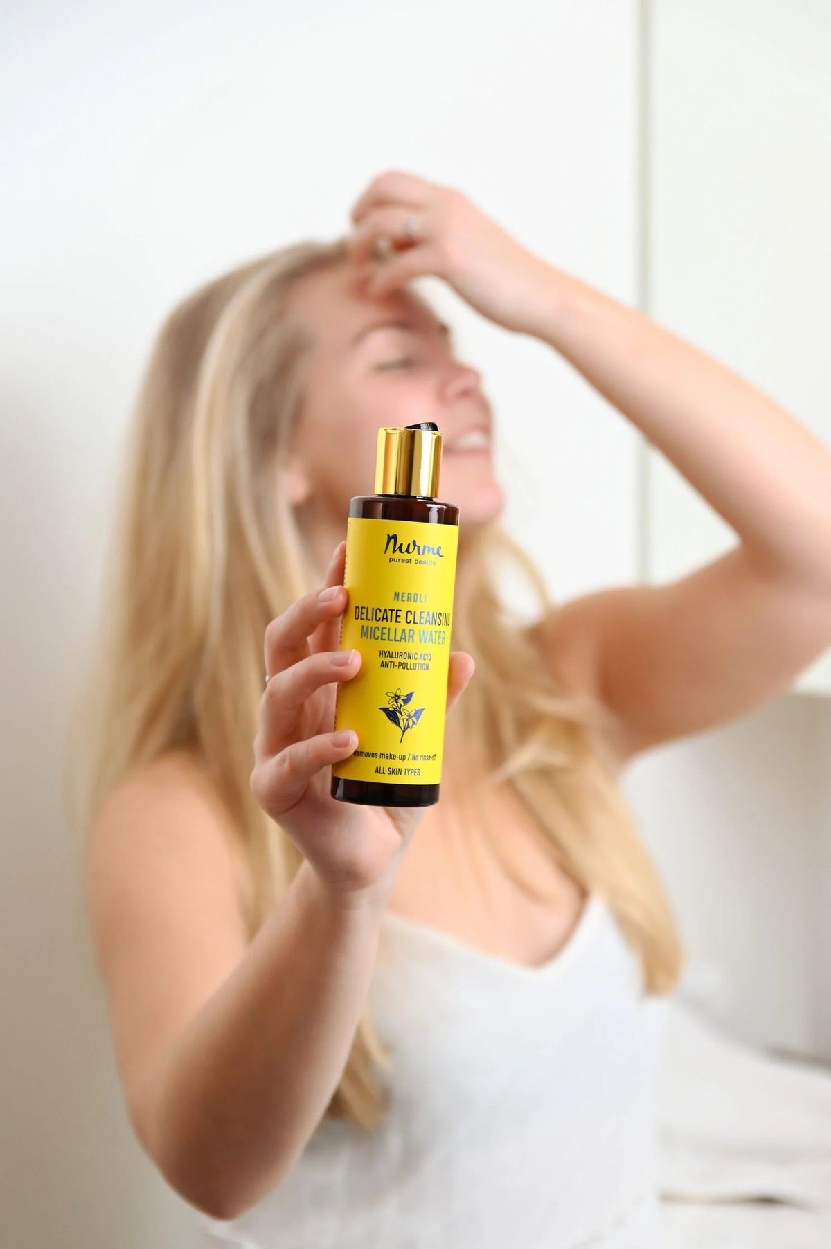 1. Woman holding Nurme Delicate Cleansing Micellar Water bottle, smiling with eyes closed, in a bright indoor setting