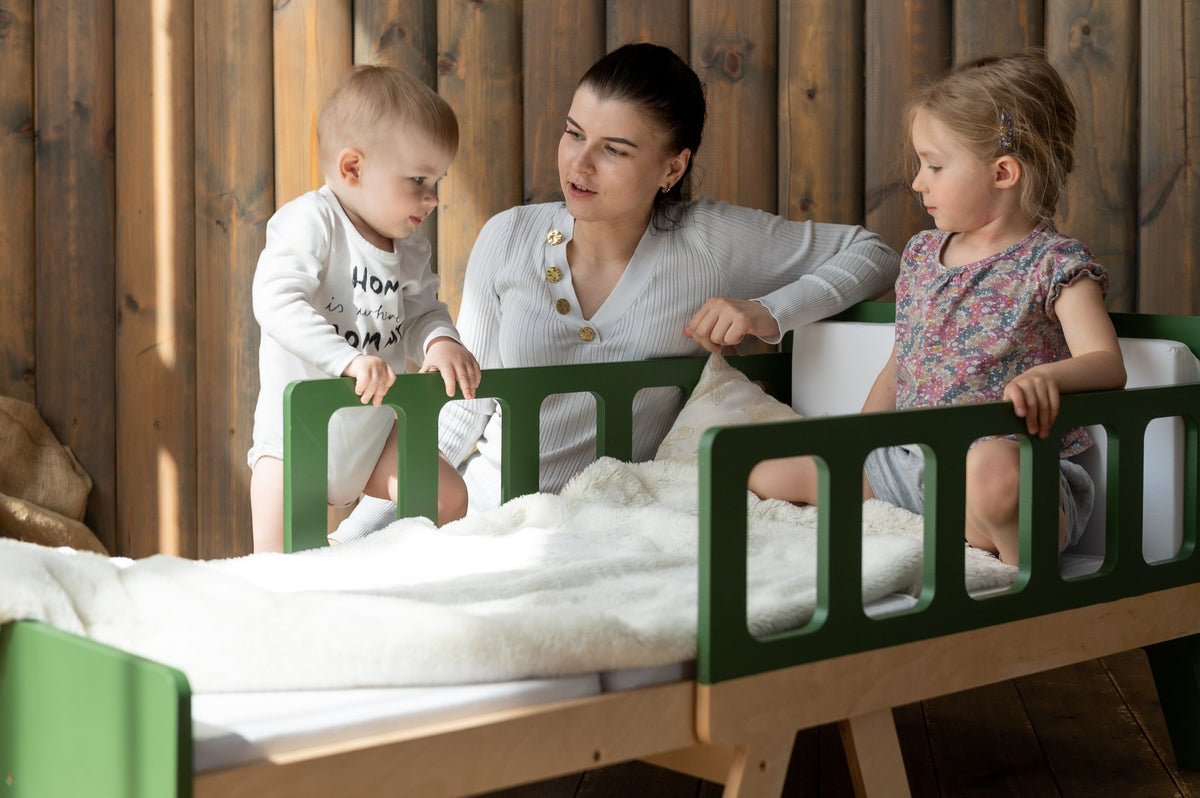 19. Woman with two children on green growing bed with white bedding in wooden room