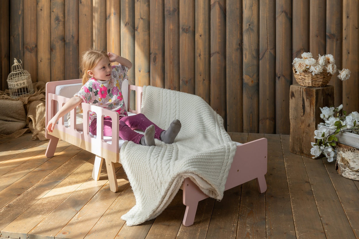 10. Child sitting on pink growing bed with white blanket in wooden room