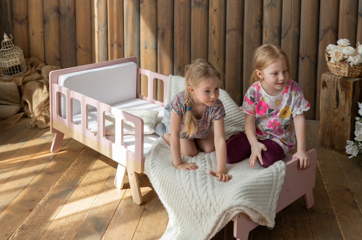 25. Two children playing on pink growing bed with white blanket in wooden room