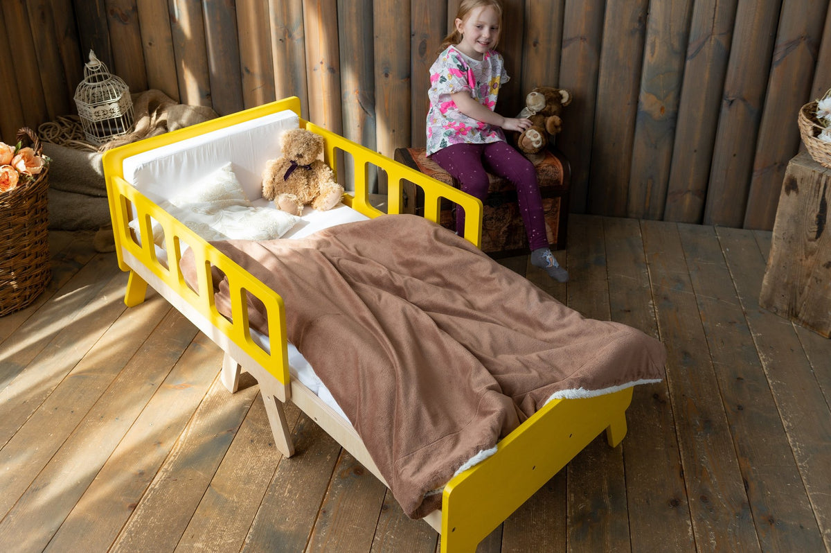 12. Child sitting on yellow growing bed with brown blanket in sunlit wooden room