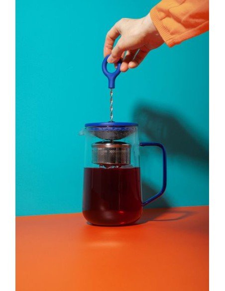 1. Person using blue and transparent Gyro teapot by La Cafetière, filled with tea, against a vibrant background