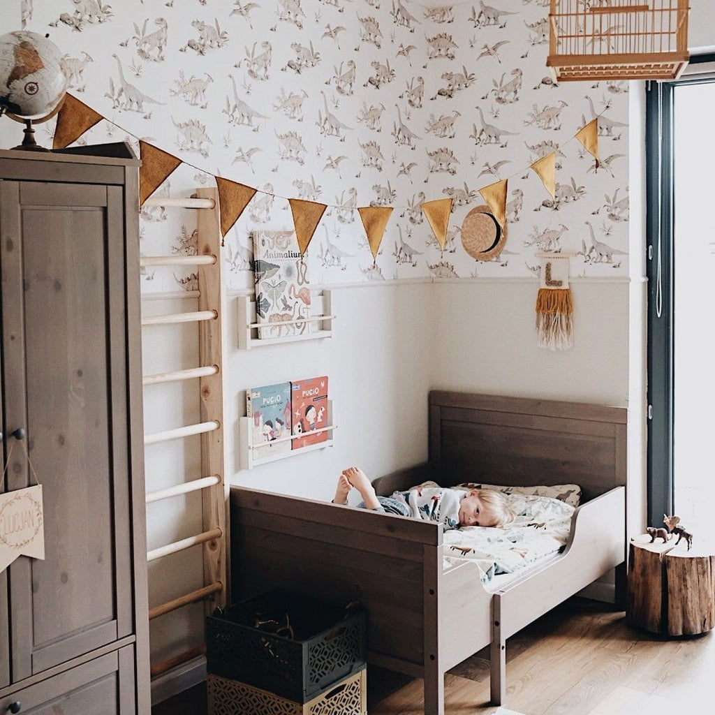 5. Child lying in bed in room with dinosaur wallpaper, wooden furniture, and decorative bunting