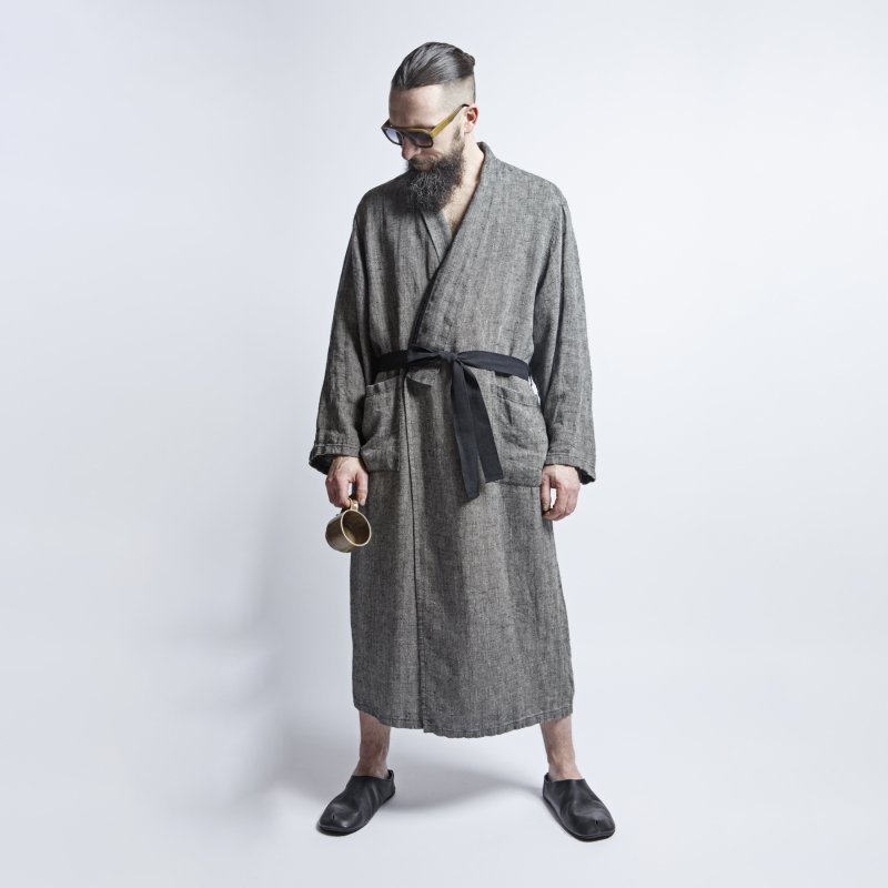 1. Man wearing grayish-black linen bathrobe with fishtail pattern and black belt, holding a mug, standing in studio setting