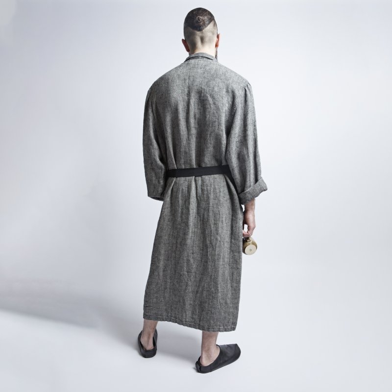 2. Back view of man in grayish-black linen bathrobe with fishtail pattern and black belt, holding a mug, in studio setting