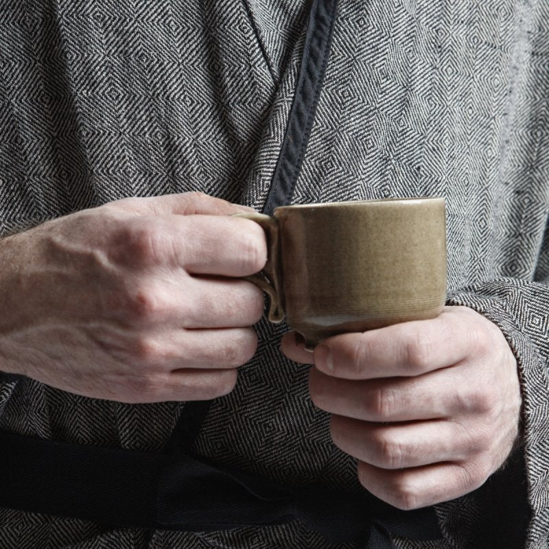 6. Close-up of hands holding a mug, wearing grayish-black linen bathrobe with fishtail pattern and black belt