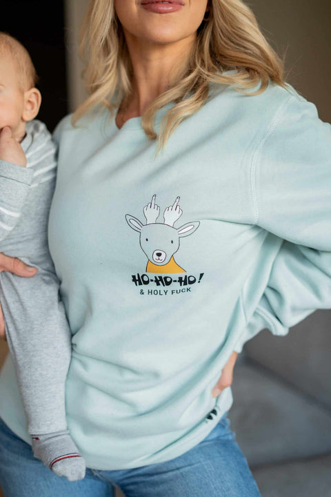 1. Woman wearing light blue oversized sweatshirt with reindeer graphic and 'Ho-Ho-Ho' text, holding a child