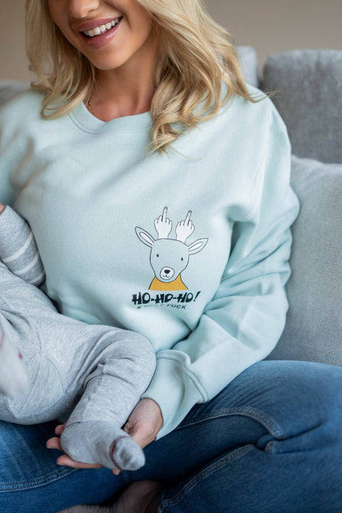 1. Woman wearing light blue oversized sweatshirt with reindeer graphic and 'Ho-Ho-Ho' text, sitting on a couch with a child