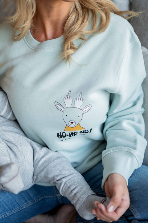 2. Woman in light blue oversized sweatshirt with reindeer graphic and 'Ho-Ho-Ho' text, sitting on a couch with a child