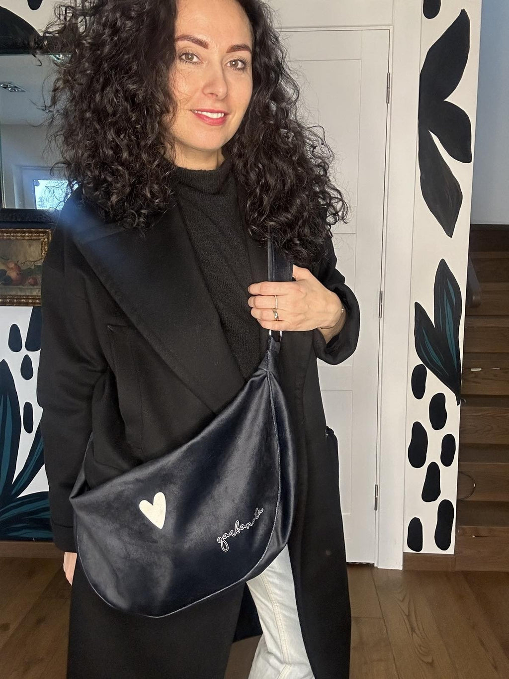 2. Woman showcasing Garbanota Hobo Bag Heart in black with heart detail, worn over shoulder indoors
