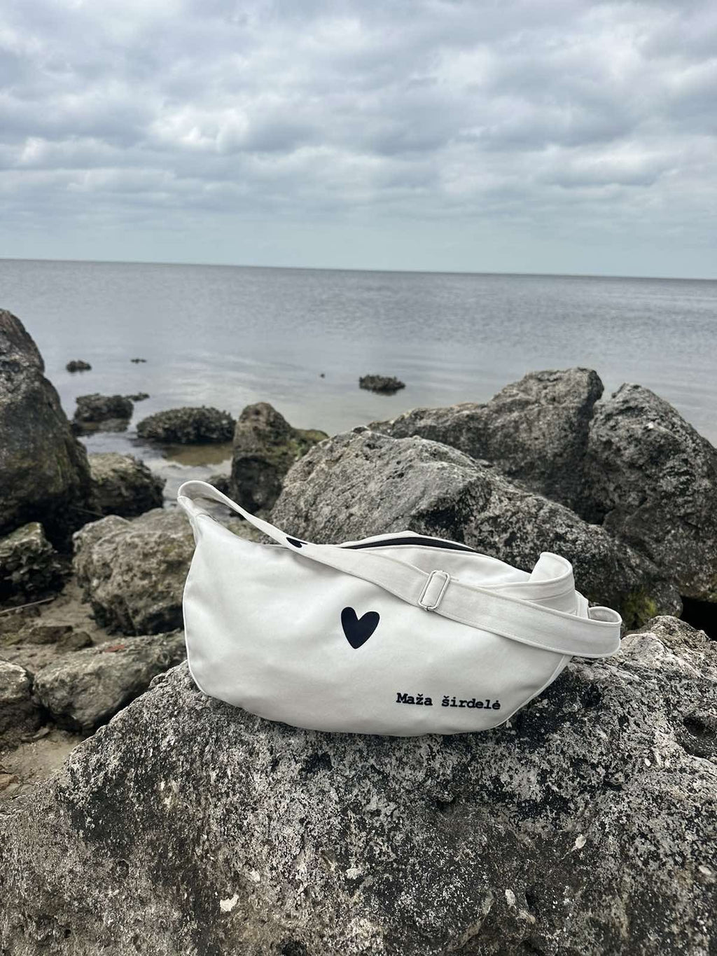 15. Garbanota Hobo Bag Heart in white hanging on wall, showcasing heart detail and adjustable strap