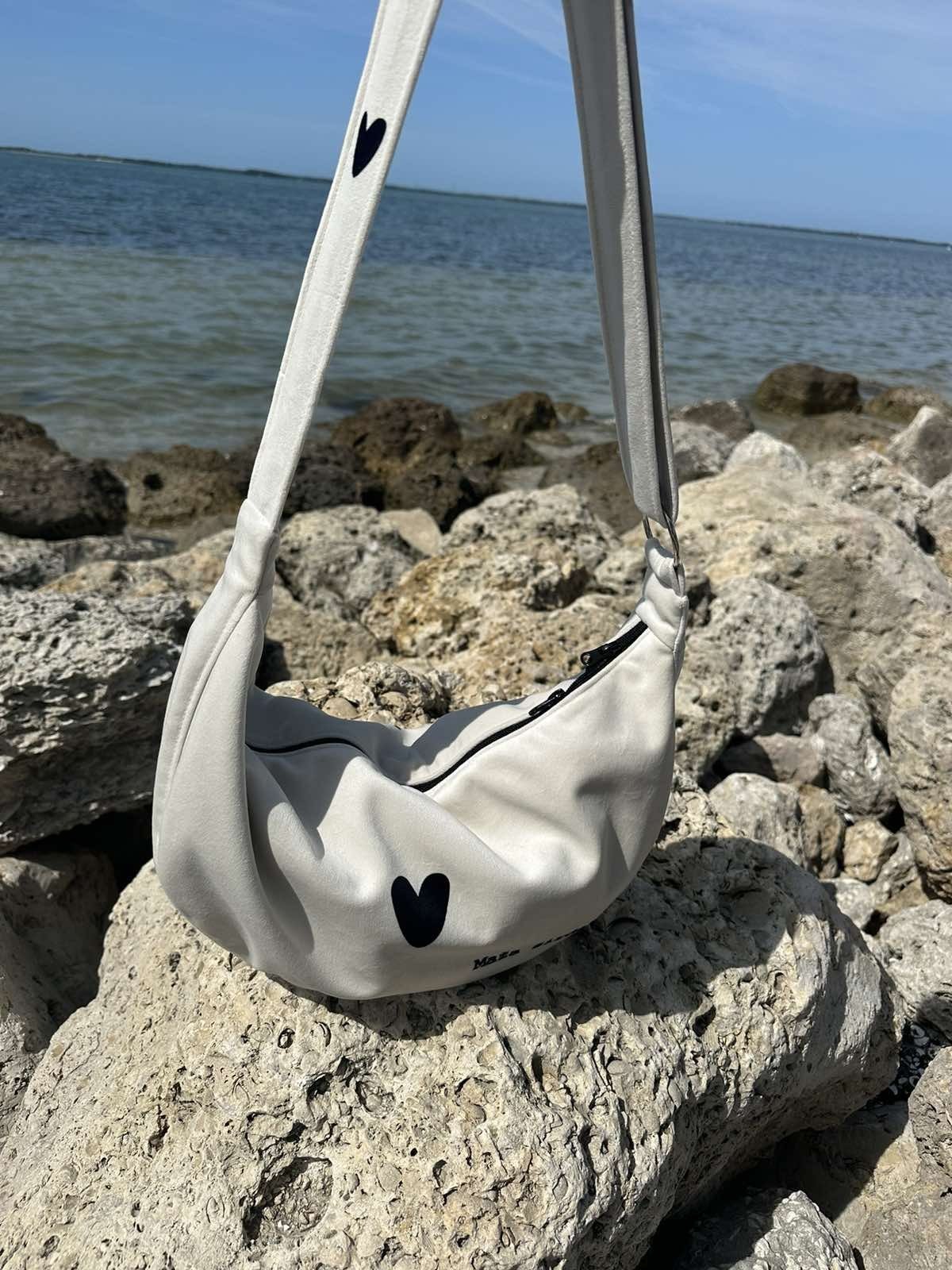 14. Garbanota Hobo Bag Heart in white on rocky beach, highlighting heart design and craftsmanship