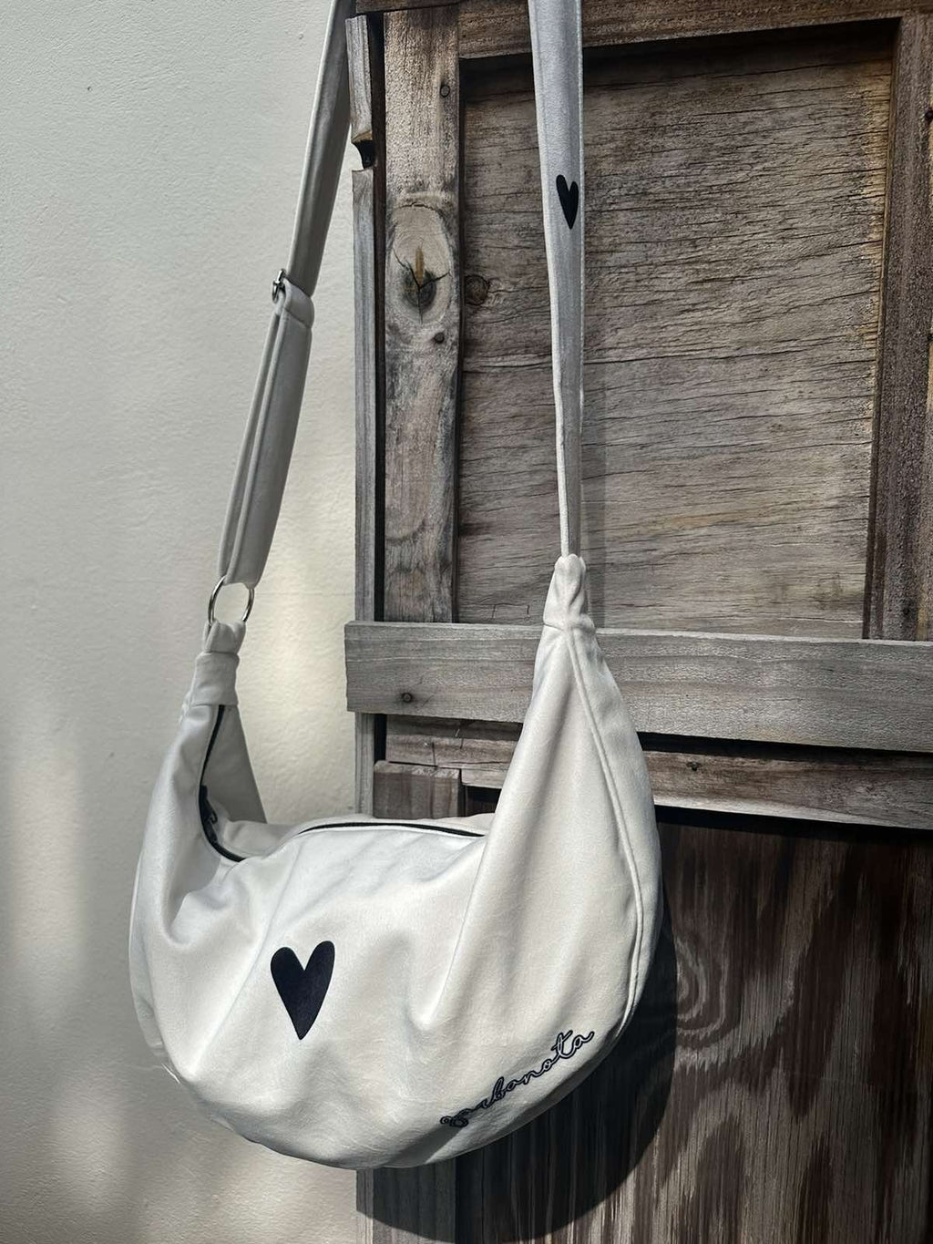 12. Garbanota Hobo Bag Heart in white hanging on wooden fence, highlighting heart design and texture