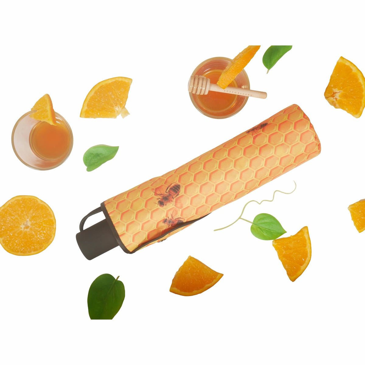 4. Flat lay of Honey Umbrella in honeycomb pattern with orange slices and leaves, highlighting compact design
