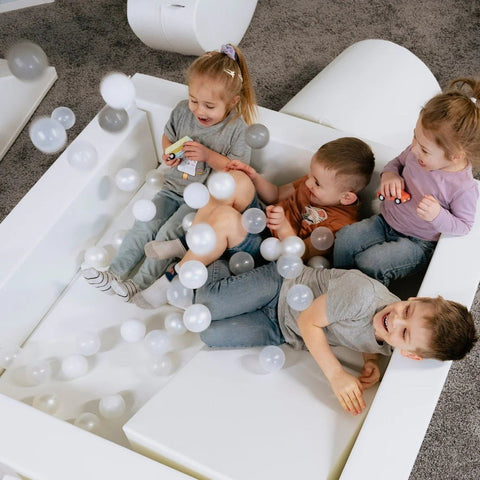 1. Three children playing in a white ball pit filled with IGLU soft play balls in pastel colors, creating a fun and sensory-rich environment