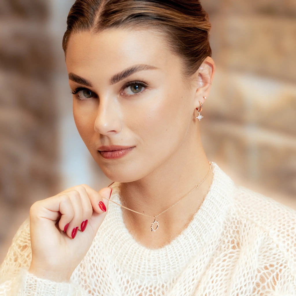 1. Woman wearing rose gold star stud earrings with zircon center, holding necklace, in cozy indoor setting