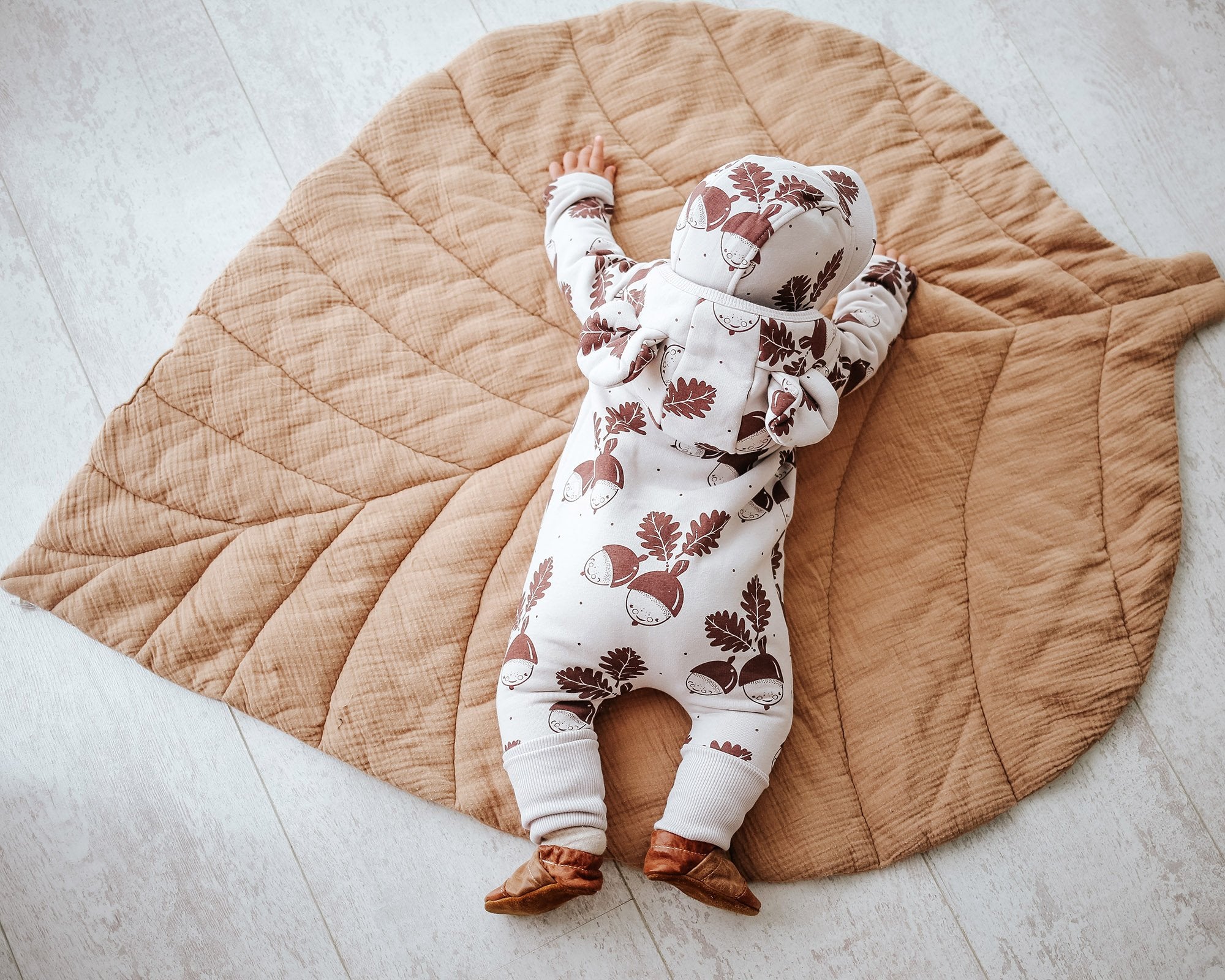 2. Baby in Zezuzulla eared jumpsuit with acorn print, lying face down on a leaf-shaped mat