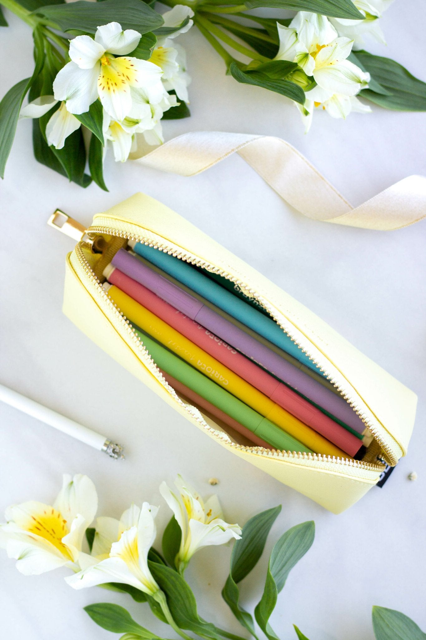 2. Open SEIK Pencil Case Sunshine in yellow, showing colorful pens inside, surrounded by flowers