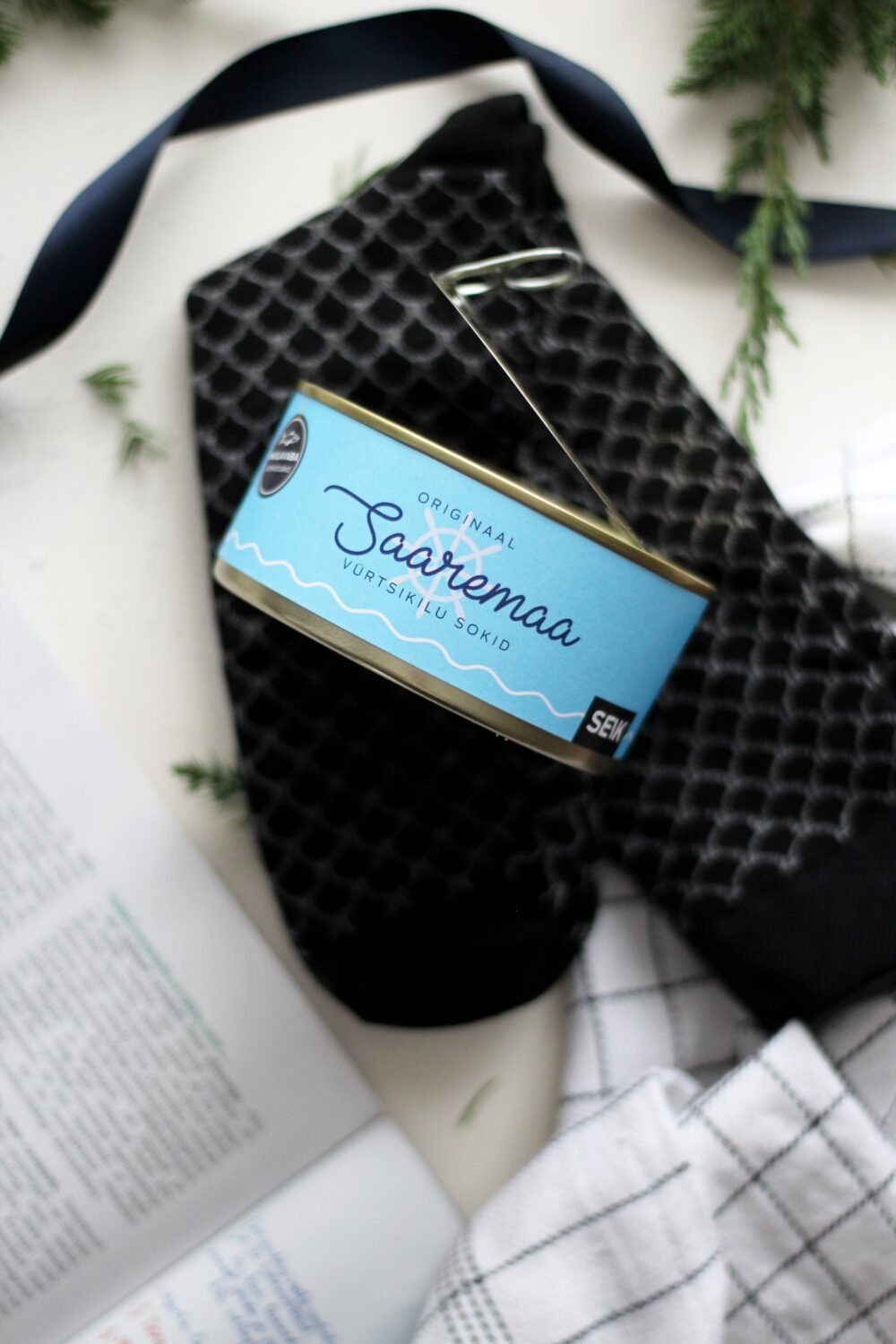 11. Saaremaa Vürtsikilu Socks with open tin, showing black pattern and SEIK branding, styled with book