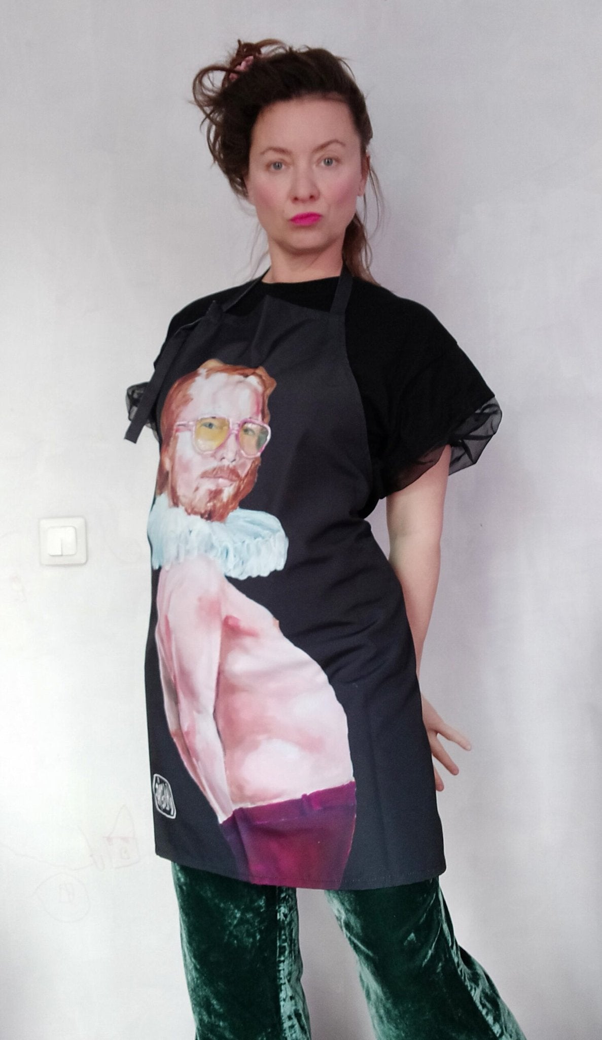 1. Woman wearing Katrin Valgemäe's 'Pervert in the Kitchen' apron with pop art design, standing against a plain wall