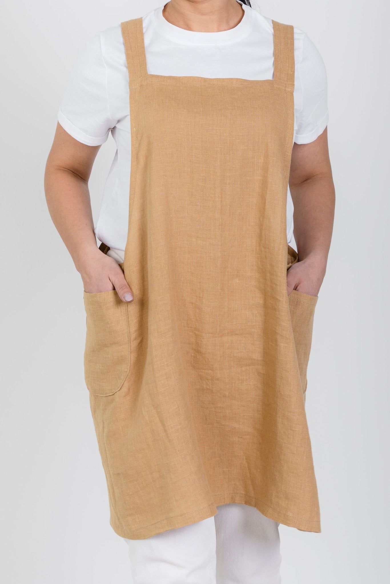9. Front view of woman wearing beige Japanese-style linen apron with pockets over white shirt
