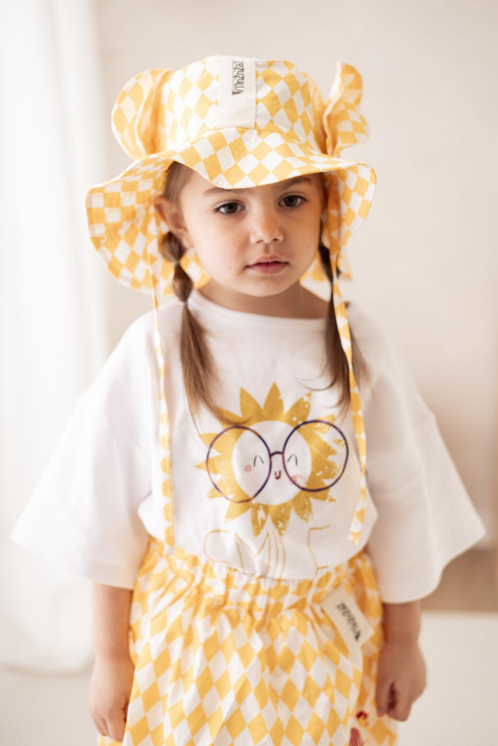 6. Child wearing yellow and white checkered hat with ears and matching outfit, standing indoors