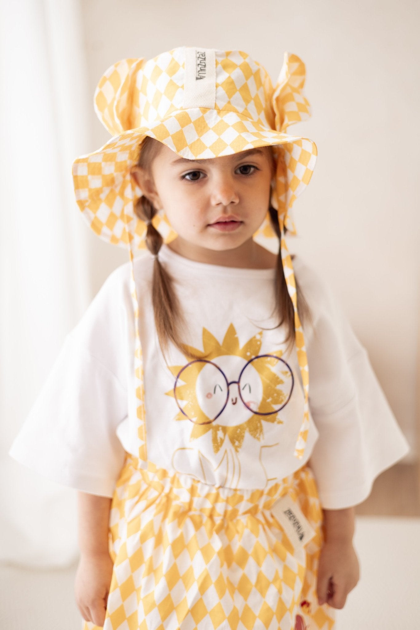 6. Child wearing yellow and white checkered hat with ears and matching outfit, standing indoors
