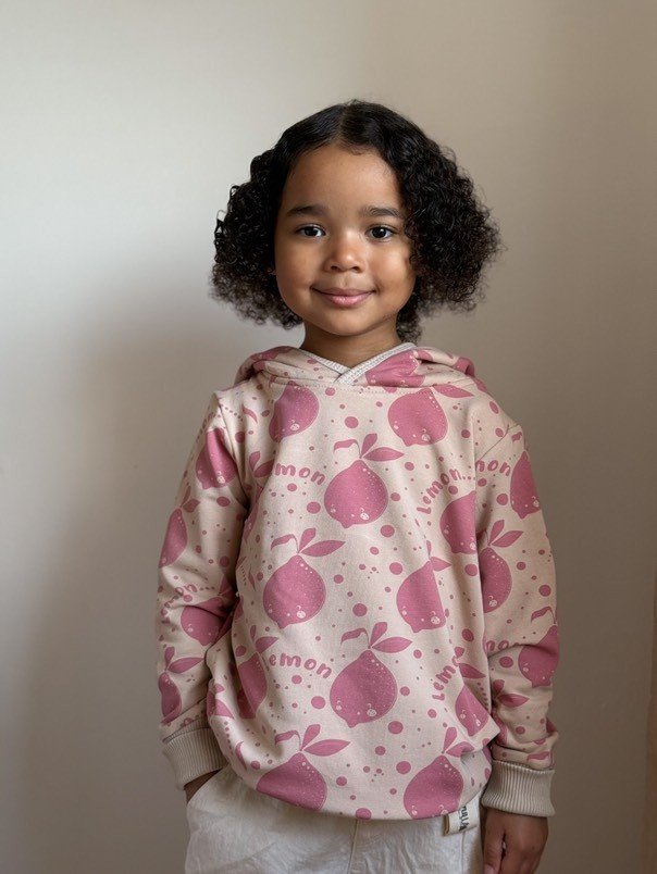 1. Child wearing Zezuzulla beige hoodie with pink lemon print and ears, smiling indoors