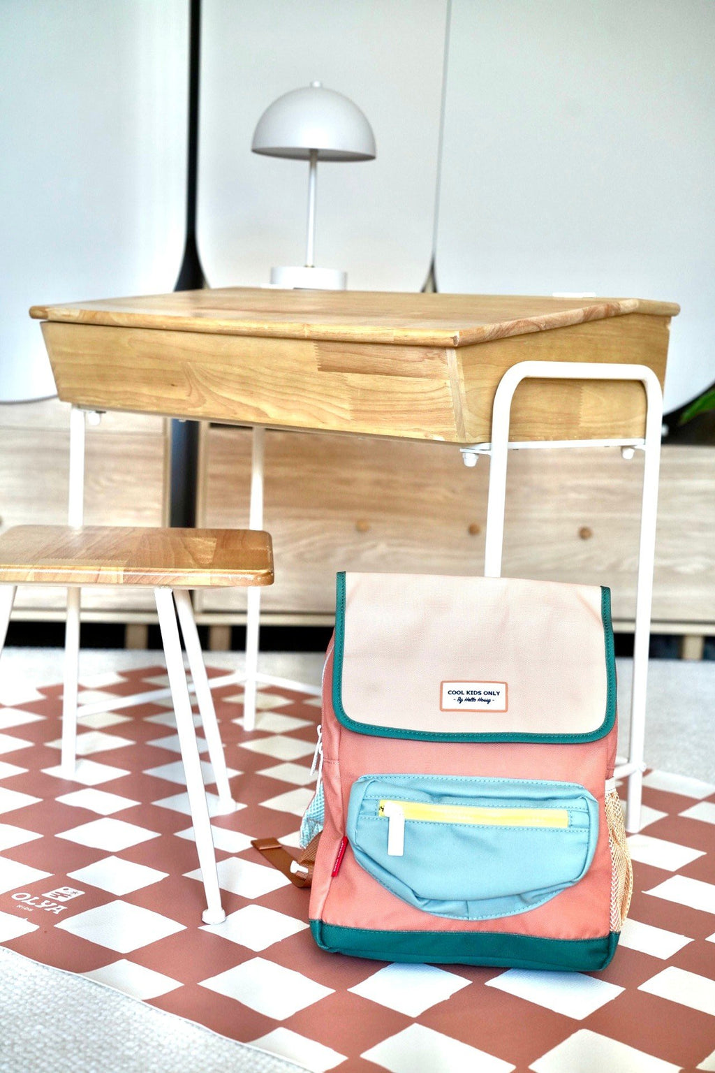 5. Pink and beige checkered floor mat with a backpack next to a wooden desk and chair