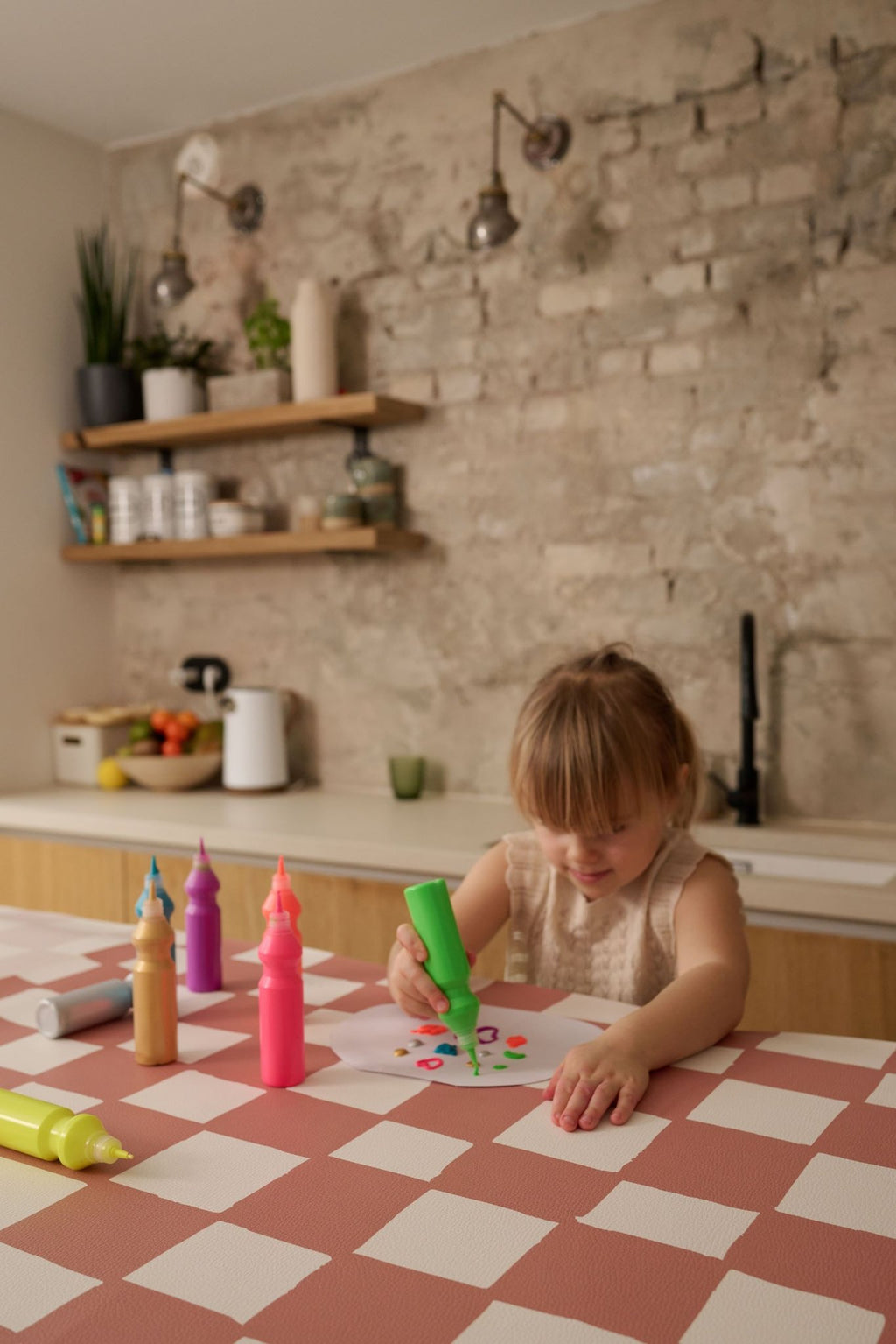 7. Girl using paint on a pink and beige checkered table cover in a rustic kitchen