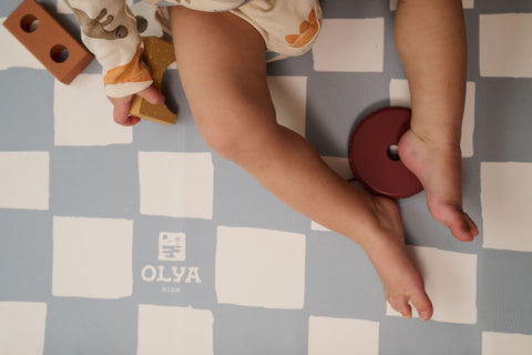 5. Child playing on blue and white checkered floor mat with OLYA KIDS logo and toy blocks